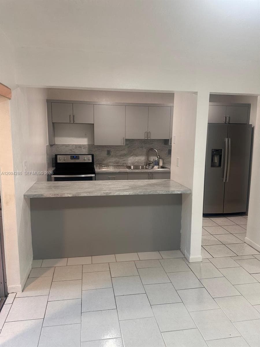 Kitchen featuring flat-panel cabinetry, stone-patterned countertops, a stainless steel side-by-side refrigerator, a stainless steel electric range, and tiled flooring
