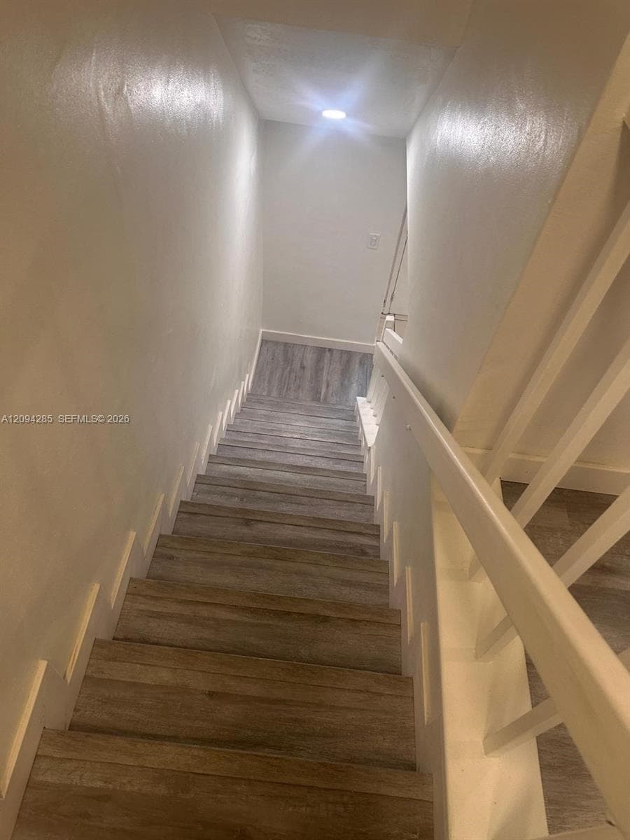 Staircase featuring wood-finish flooring, white painted walls, recessed lighting, and a white wooden railing