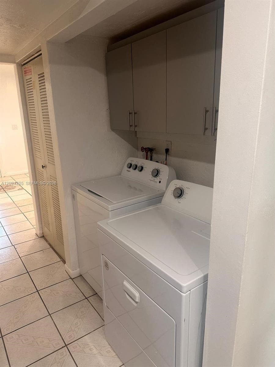 Laundry area featuring light-toned upper cabinetry, neutral ceramic tile flooring, and louvered closet doors