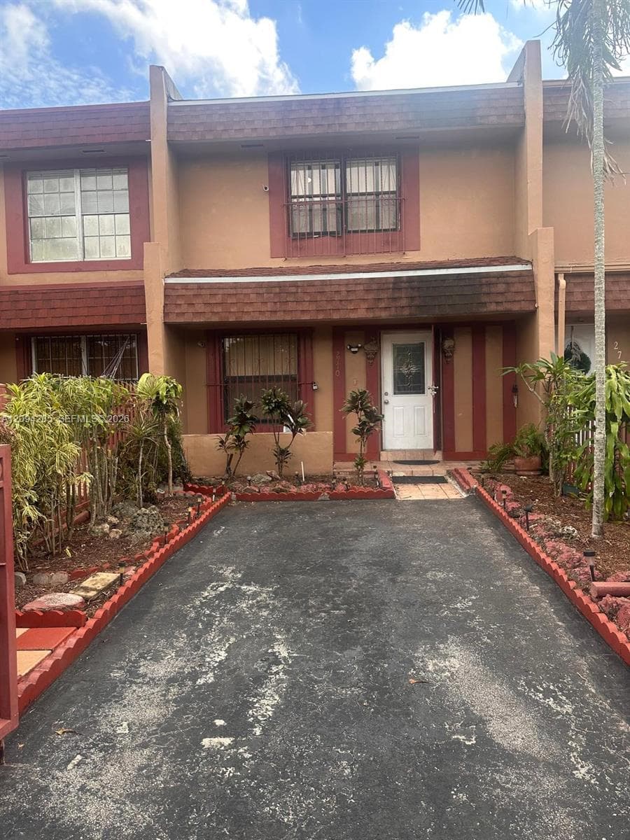 Two-story exterior featuring a shingle roofline, decorative masonry accents, and a paved driveway bordered by stone landscape edging