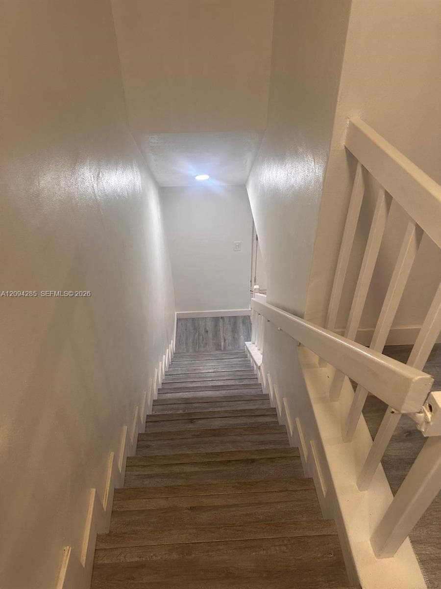 Staircase featuring wood-finish flooring, white painted walls, and a white balustrade with a matching handrail