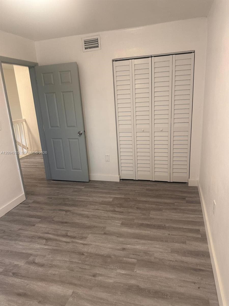 Wood-finish flooring, six-panel interior door, and white louvered bifold closet doors