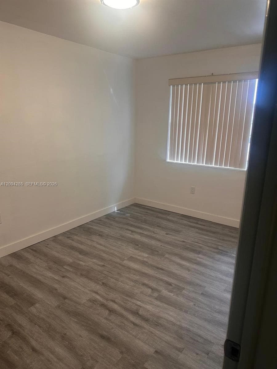 Room interior featuring neutral walls, wood-finish flooring, and a window fitted with vertical blinds