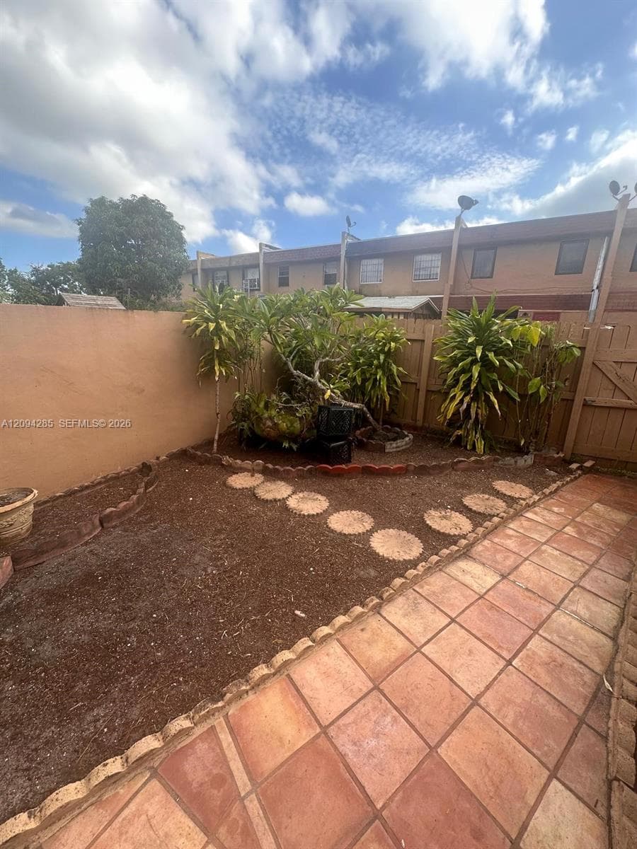 Private rear courtyard featuring a tile patio, mulched garden beds with decorative edging, concrete paver stones, and perimeter wood fencing