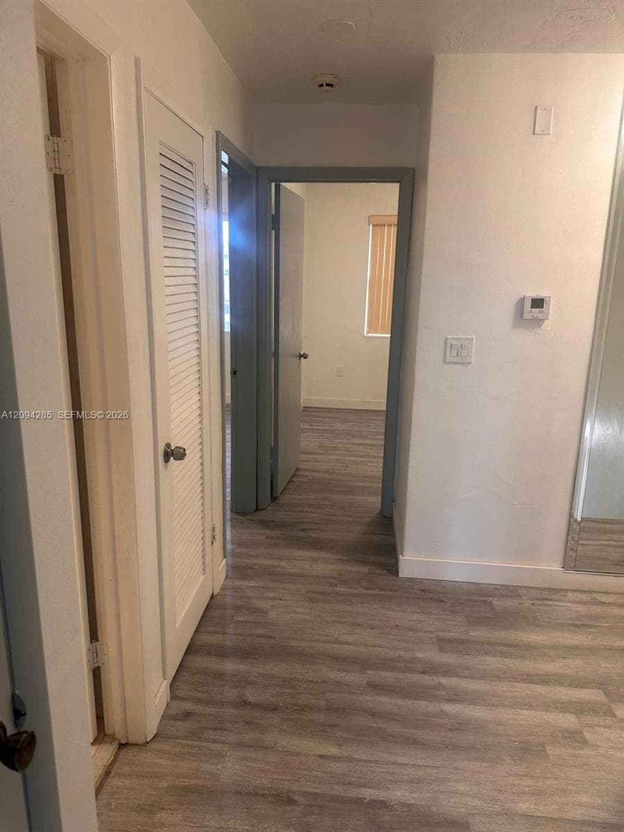 Hallway featuring wood-finish flooring, white walls, and a louvered closet door