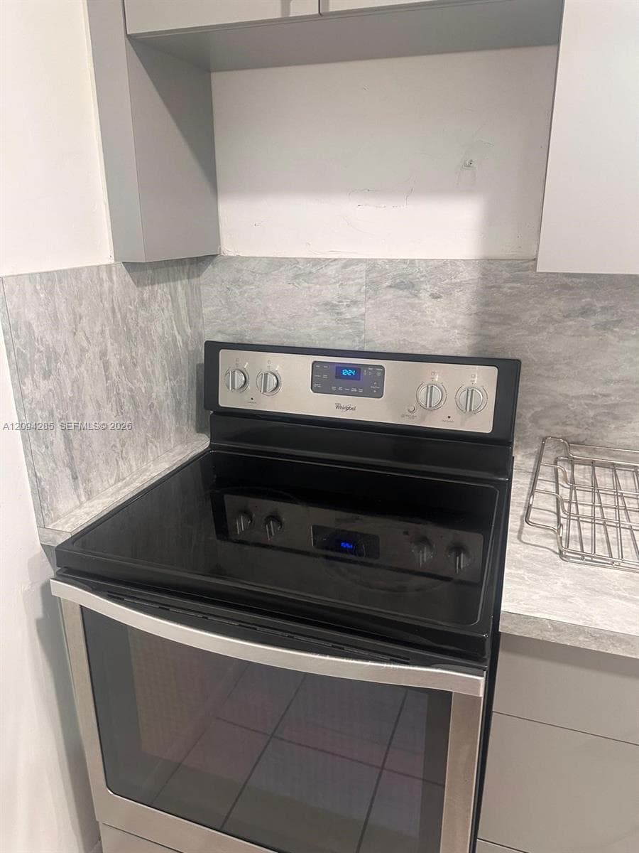 Stainless steel Whirlpool range with digital control panel, stone-finish countertops, stone-patterned backsplash, and flat-panel cabinetry