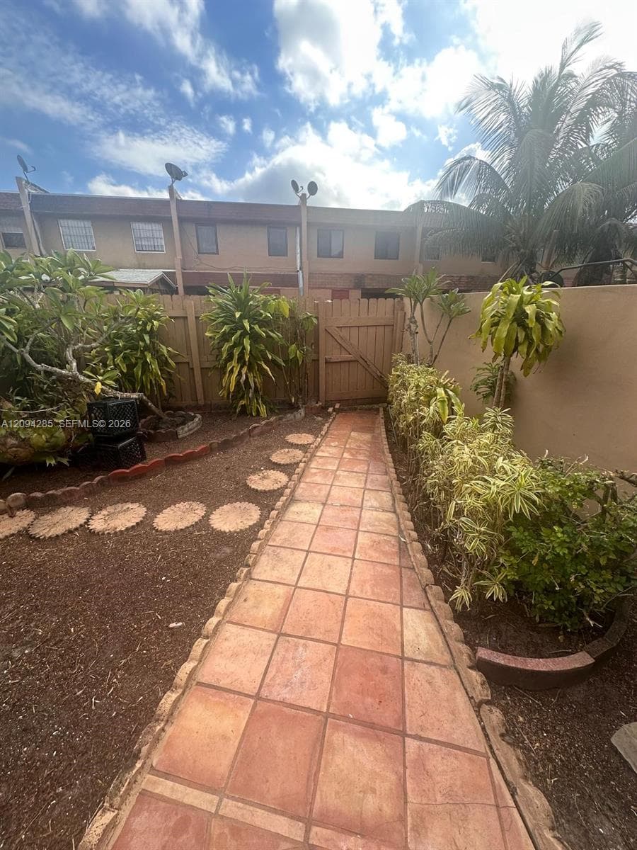 Outdoor walkway featuring terra-cotta tile paving, wood perimeter fencing, and landscaped garden beds