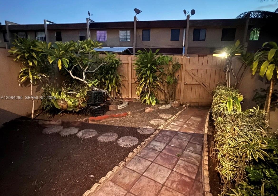Private outdoor space featuring a paved tile walkway, decorative stone path, perimeter wood fencing, and mature landscaping