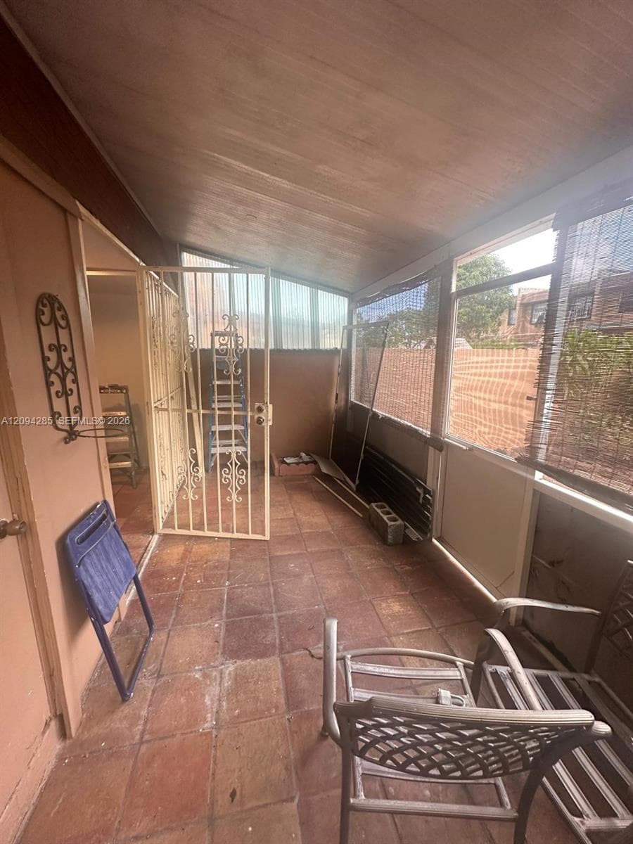 Enclosed porch featuring terra cotta tile flooring, a slanted ceiling, and a decorative metal security gate