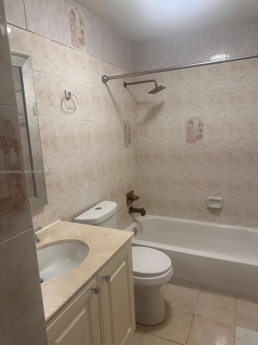 Full-wall tiled bathroom featuring a tub-shower combination, vanity with integrated basin, stone-finish countertop, and wall-mounted metal fixtures