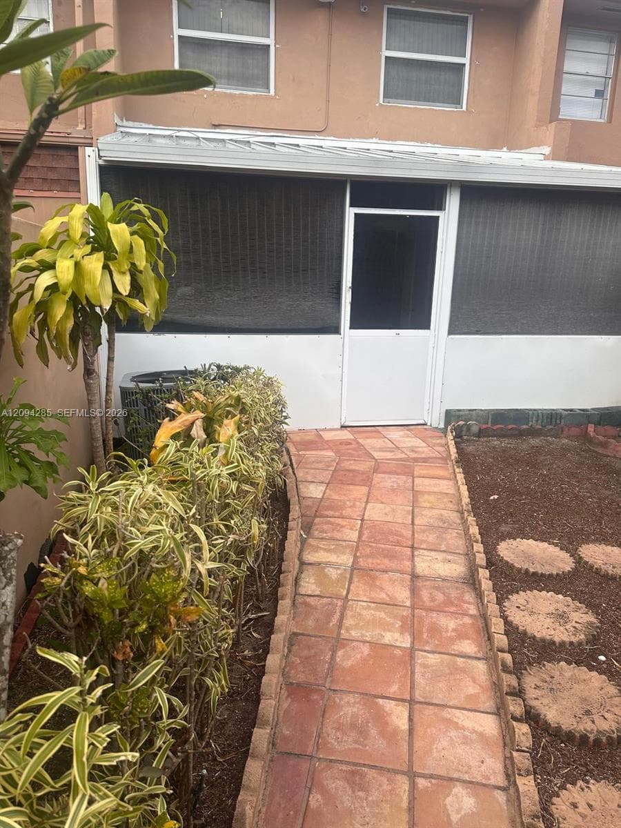 Screened-in patio with a tiled walkway, exterior stucco siding, and built-in landscape bordering