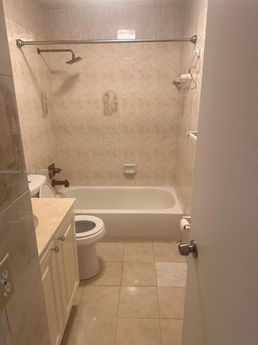 Bathroom featuring tile flooring, a tub-shower combination with full-height tile surround, wall-mounted shower head, and a vanity with a stone-top surface