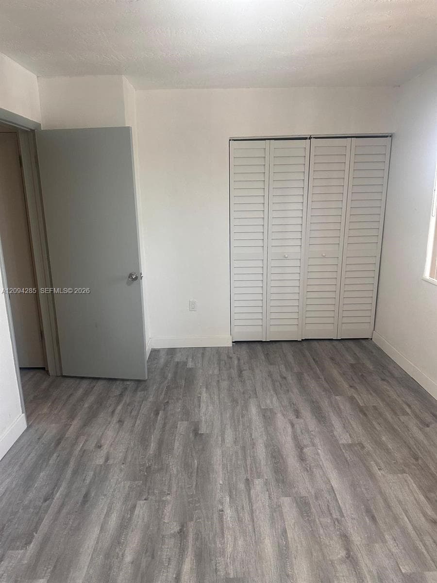 Room featuring wood-finish flooring, white louvered-style closet doors, and neutral wall tones