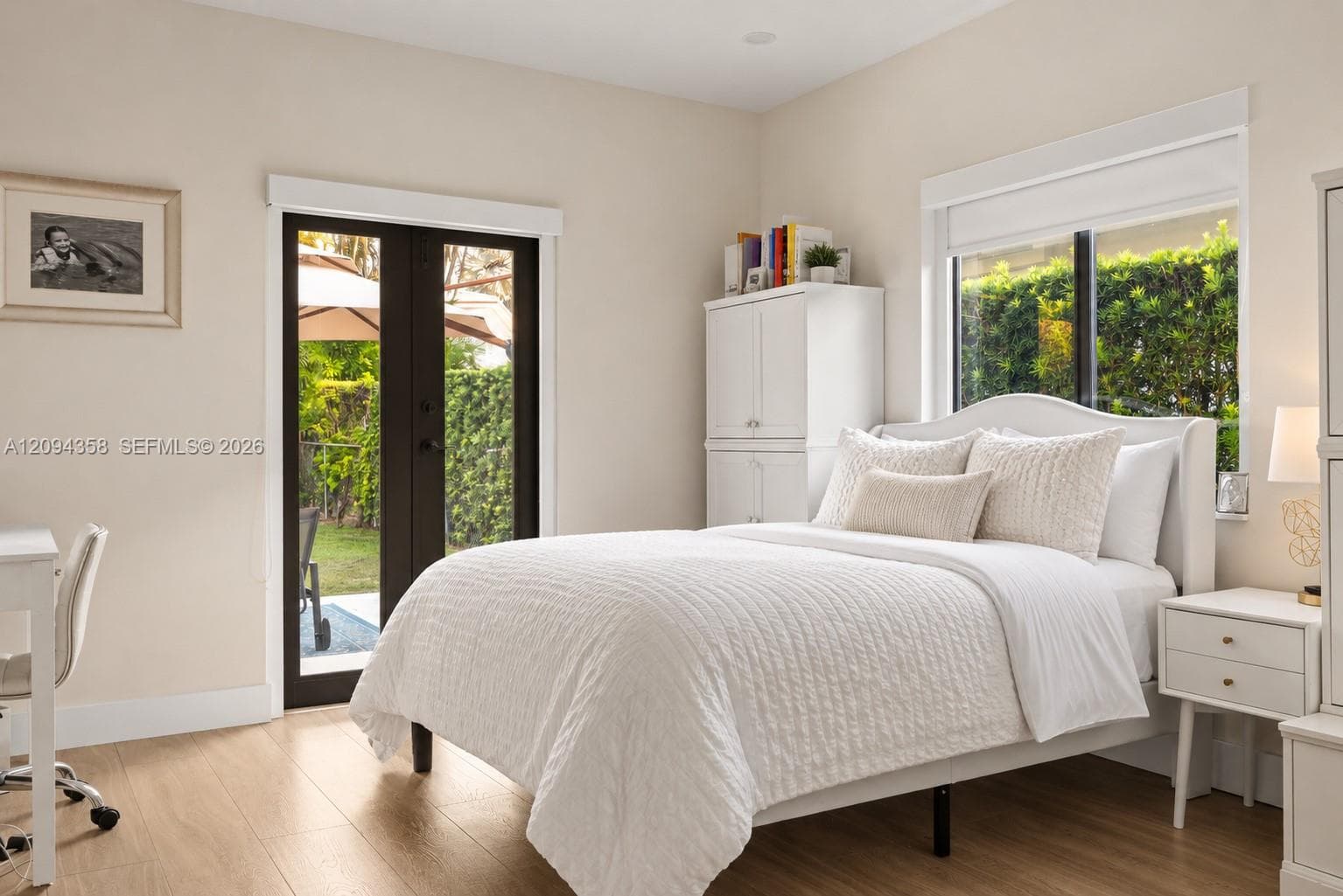 Light-filled room featuring wood-finish flooring, a white built-in storage cabinet, and black-framed French doors opening to an outdoor area