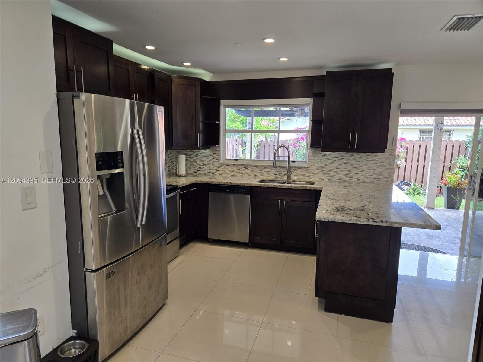 Kitchen featuring dark wood cabinetry, stainless steel appliances, stone countertops, a mosaic tile backsplash, and ceramic tile flooring