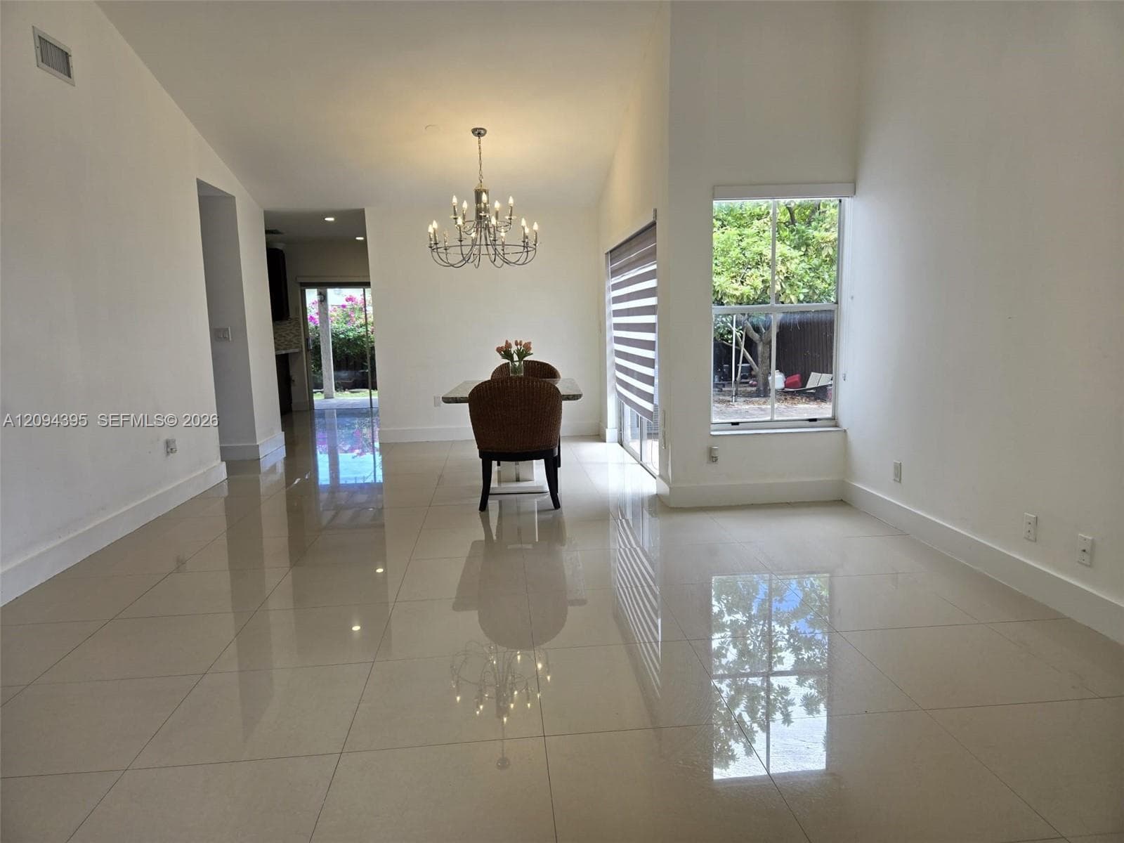 Open-concept room featuring vaulted ceilings, polished tile flooring, a multi-arm chandelier, and large windows