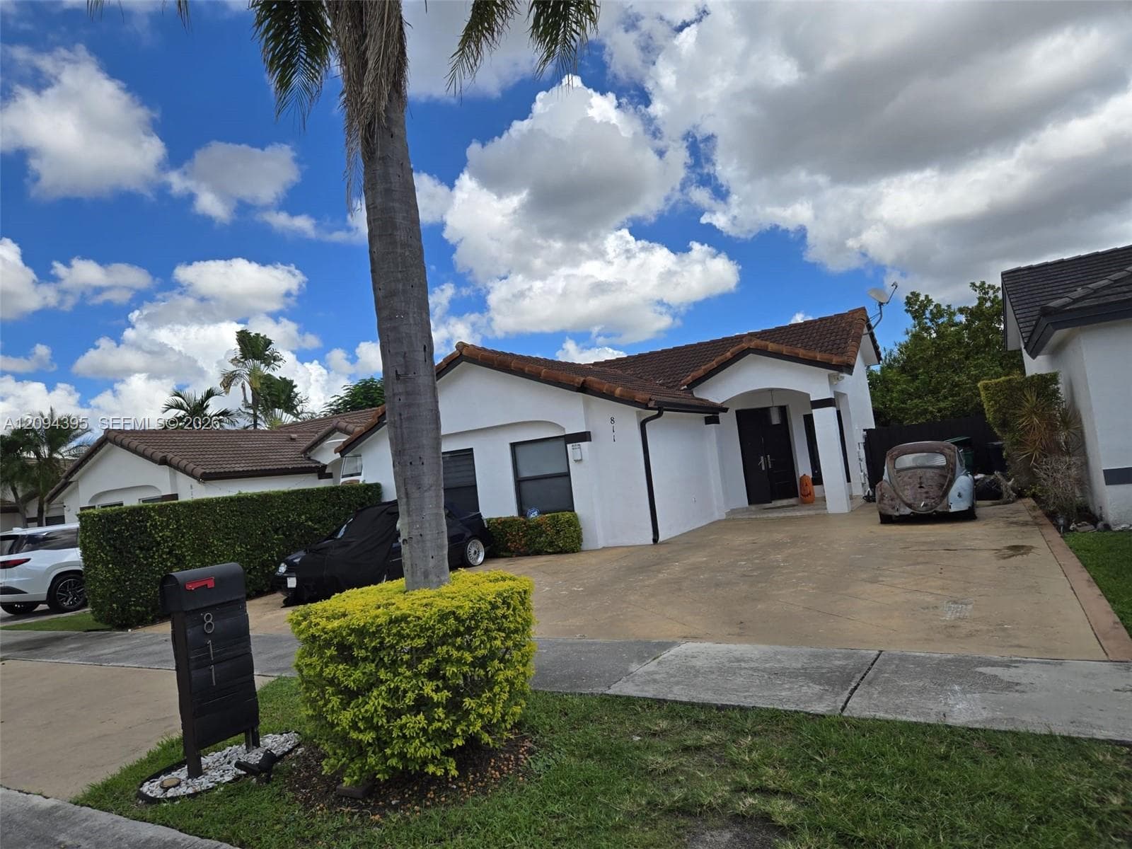 Single-story exterior featuring white stucco siding, a tiled roof, a covered entryway, and a concrete driveway