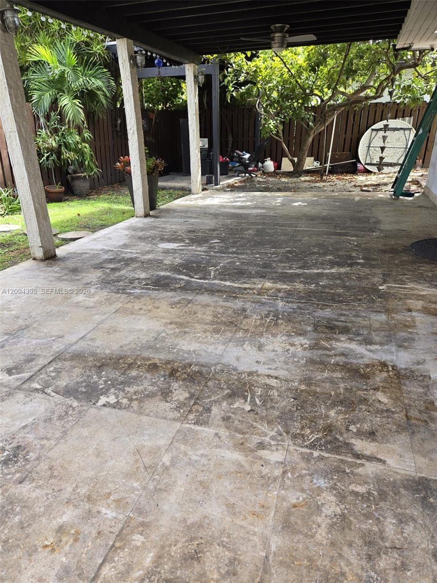 Covered concrete patio featuring a support pillar structure, ceiling fan, and perimeter wood fencing