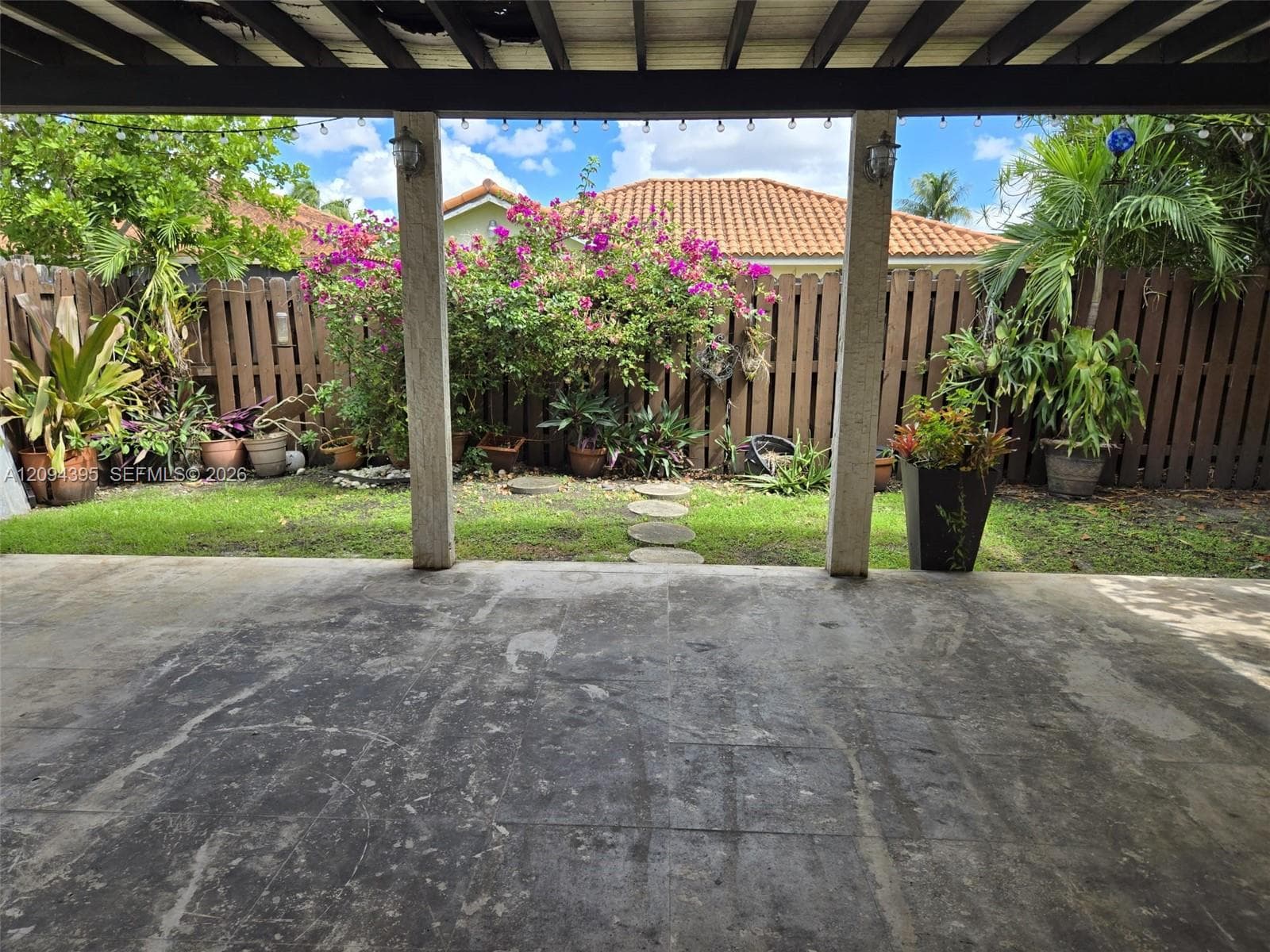 Covered patio featuring concrete flooring, structural support columns, and wood-slat privacy fencing