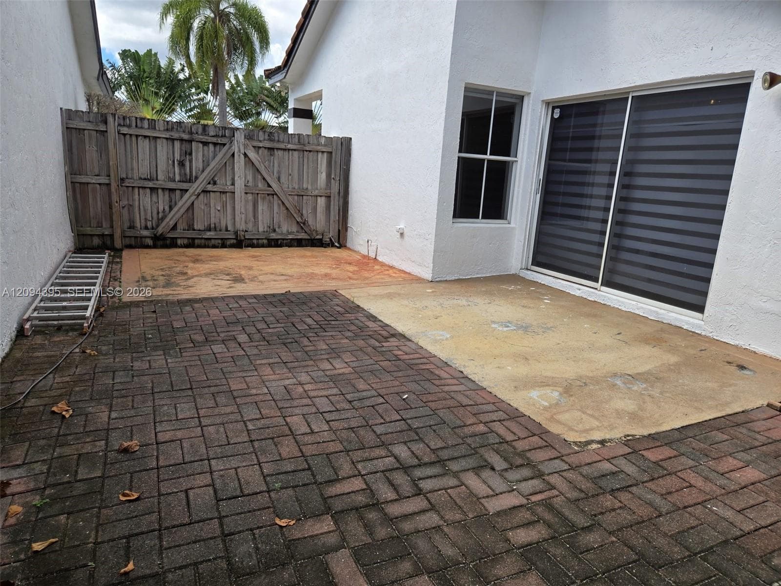 Exterior patio featuring a herringbone-patterned brick paver surface, a concrete slab area, and a wood privacy fence