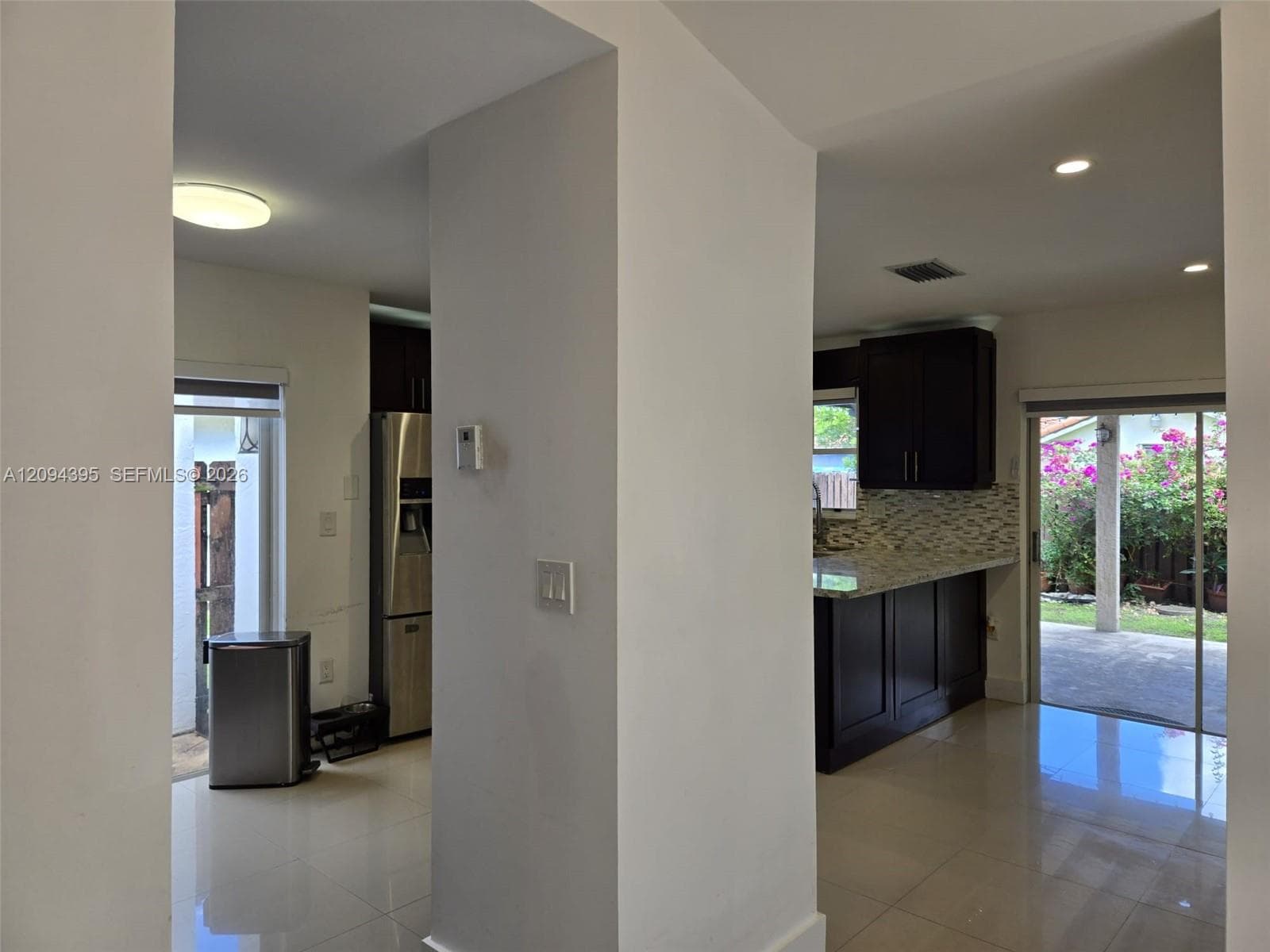 Kitchen featuring dark wood cabinetry, stone countertops, a mosaic tile backsplash, stainless steel appliances, and large-format tile flooring