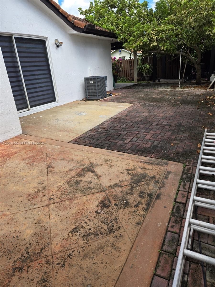 Rear exterior featuring a multi-textured patio with stamped concrete and herringbone-patterned brick pavers, a sliding glass door, and white stucco siding
