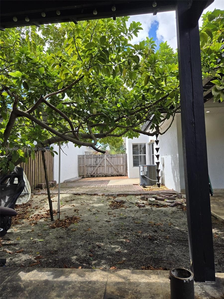 Backyard area featuring a covered pergola, brick paver patio, wood fencing, and mature trees