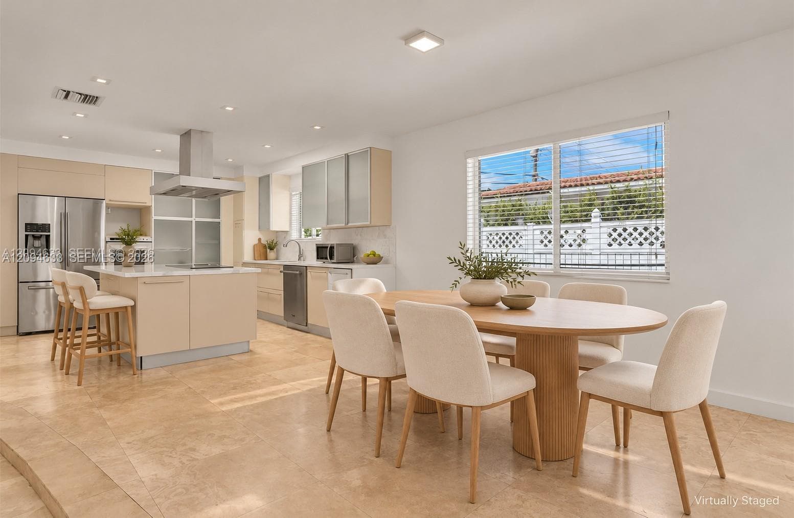 Kitchen featuring light-toned flat-panel cabinetry, a central island with quartz countertop, stainless steel appliances, a mounted range hood, and large-format stone flooring