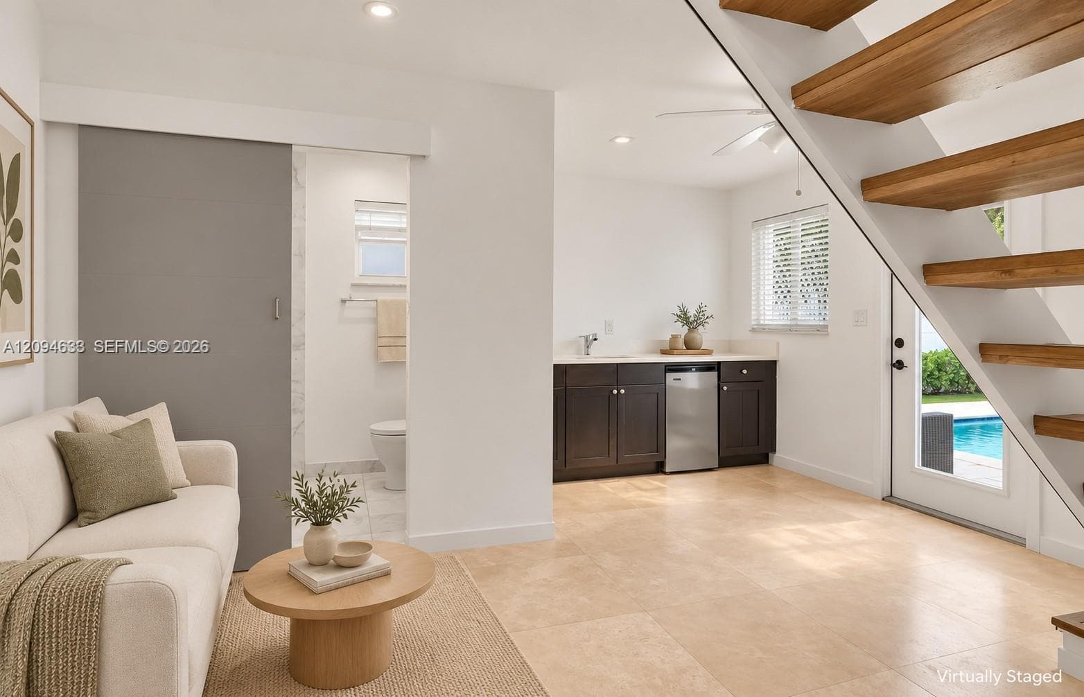 Floating staircase with wood treads, sliding barn door, dark cabinetry with stainless steel dishwasher, and large-format tile flooring