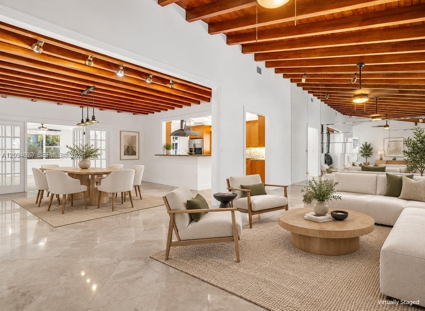 Open concept interior featuring high ceilings with exposed wood beams, polished stone flooring, recessed track lighting, and a kitchen pass-through window with an integrated breakfast bar