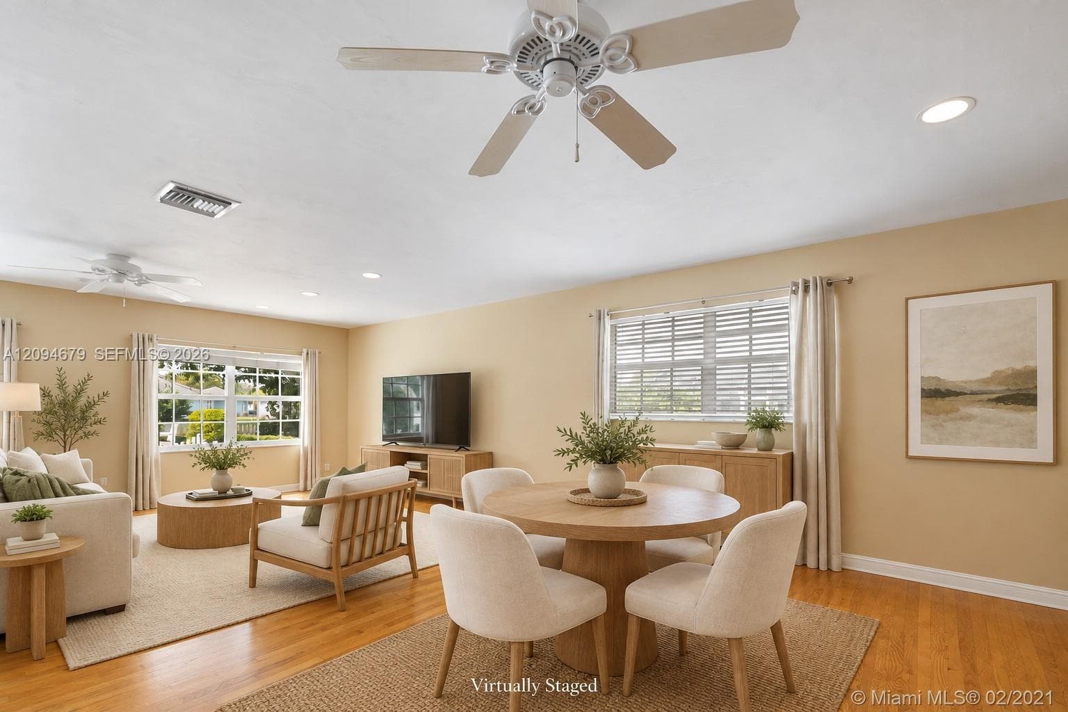 Spacious living area featuring wood-finish flooring, dual ceiling fans, and multiple large windows with horizontal blinds