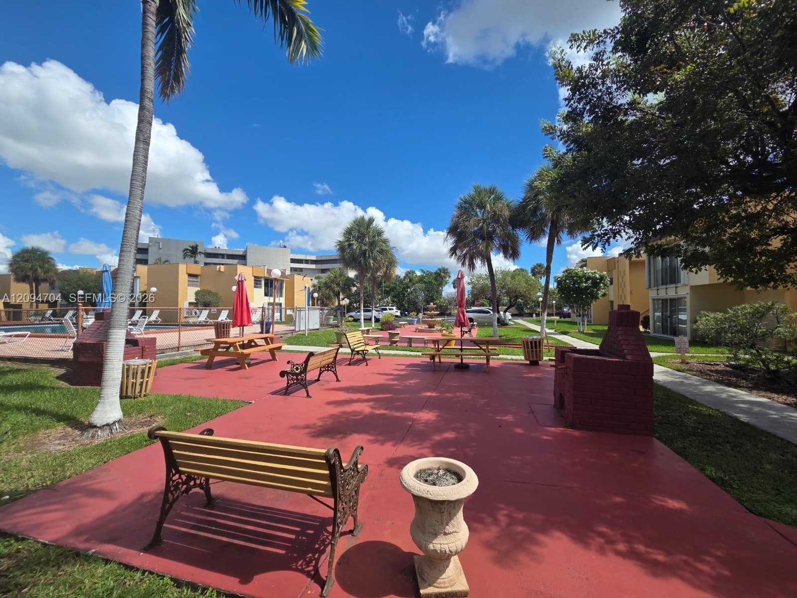 Outdoor courtyard featuring a paved recreation area, brick-built barbecue stations, and palm tree landscaping