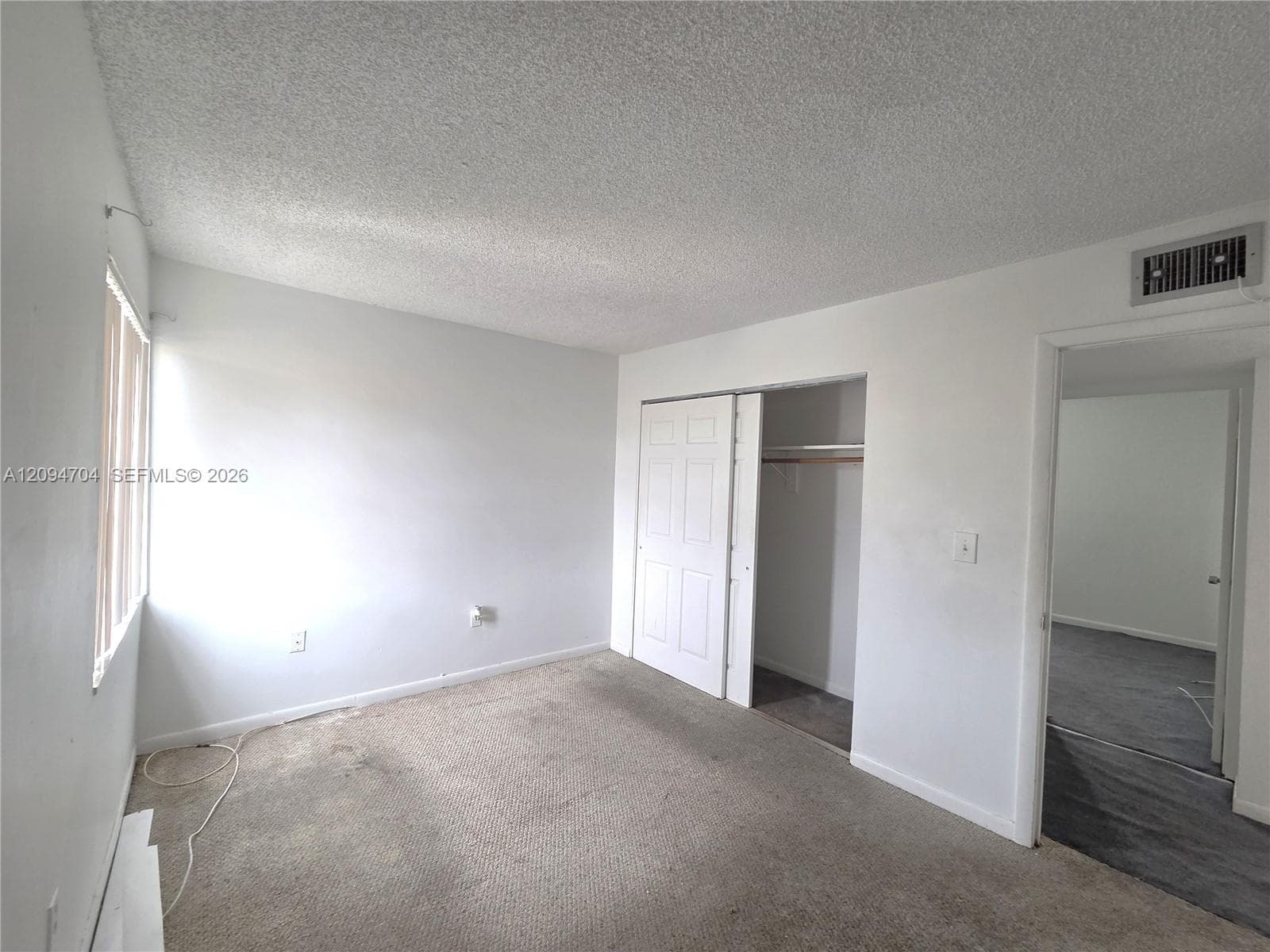 Interior space featuring neutral-toned carpeting, textured ceiling, and a closet with six-panel sliding doors
