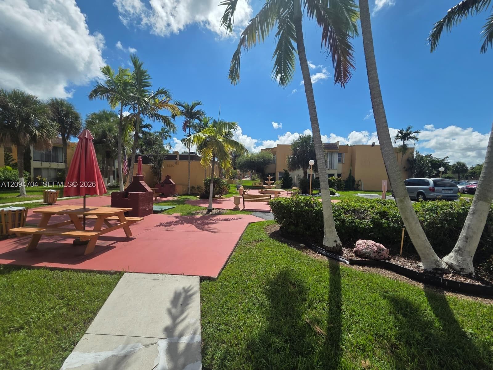 Outdoor area featuring a paved patio surface, manicured lawn, mature palm trees, decorative shrubbery, and built-in masonry structures