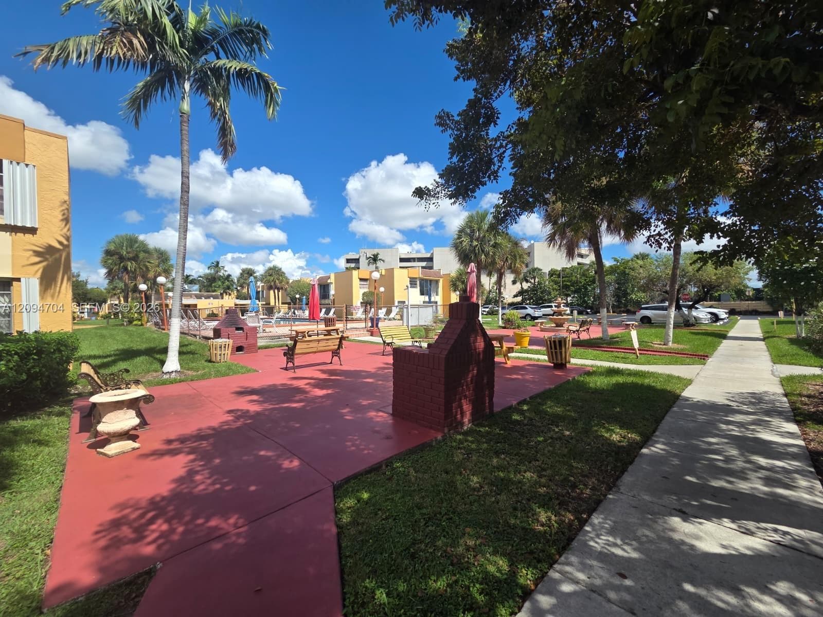 Common area featuring a paved courtyard, brick masonry barbeque grills, mature palm trees, manicured lawns, and concrete pathways