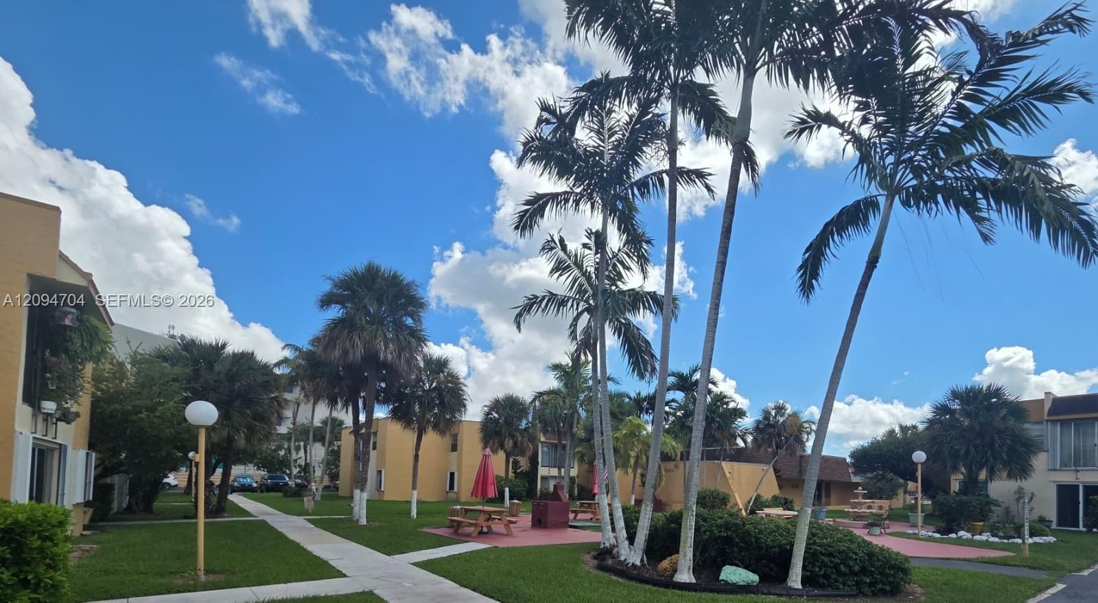 Landscaped grounds featuring mature palm trees, manicured lawns, paved walkways, and dedicated hardscaped recreation areas