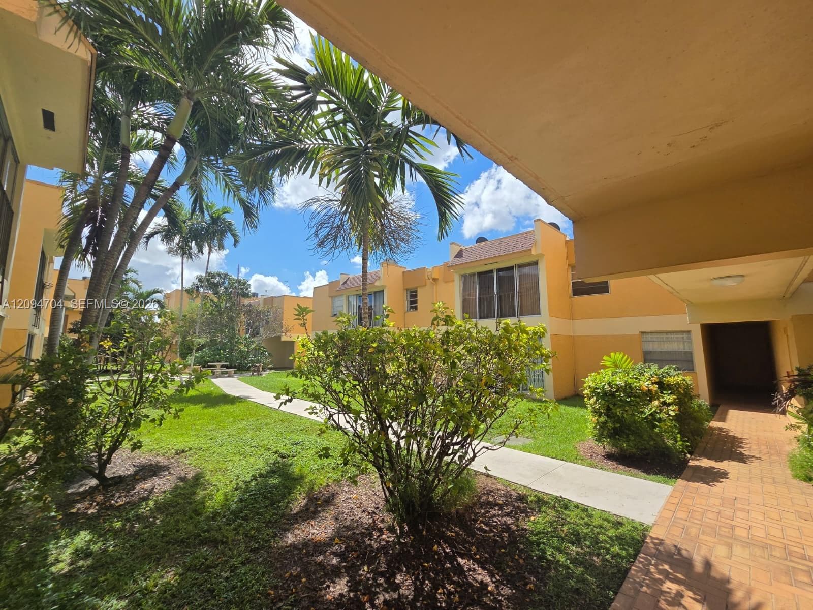 Exterior courtyard featuring mature palm trees, manicured lawn, concrete walking paths, and brick-style paved walkways