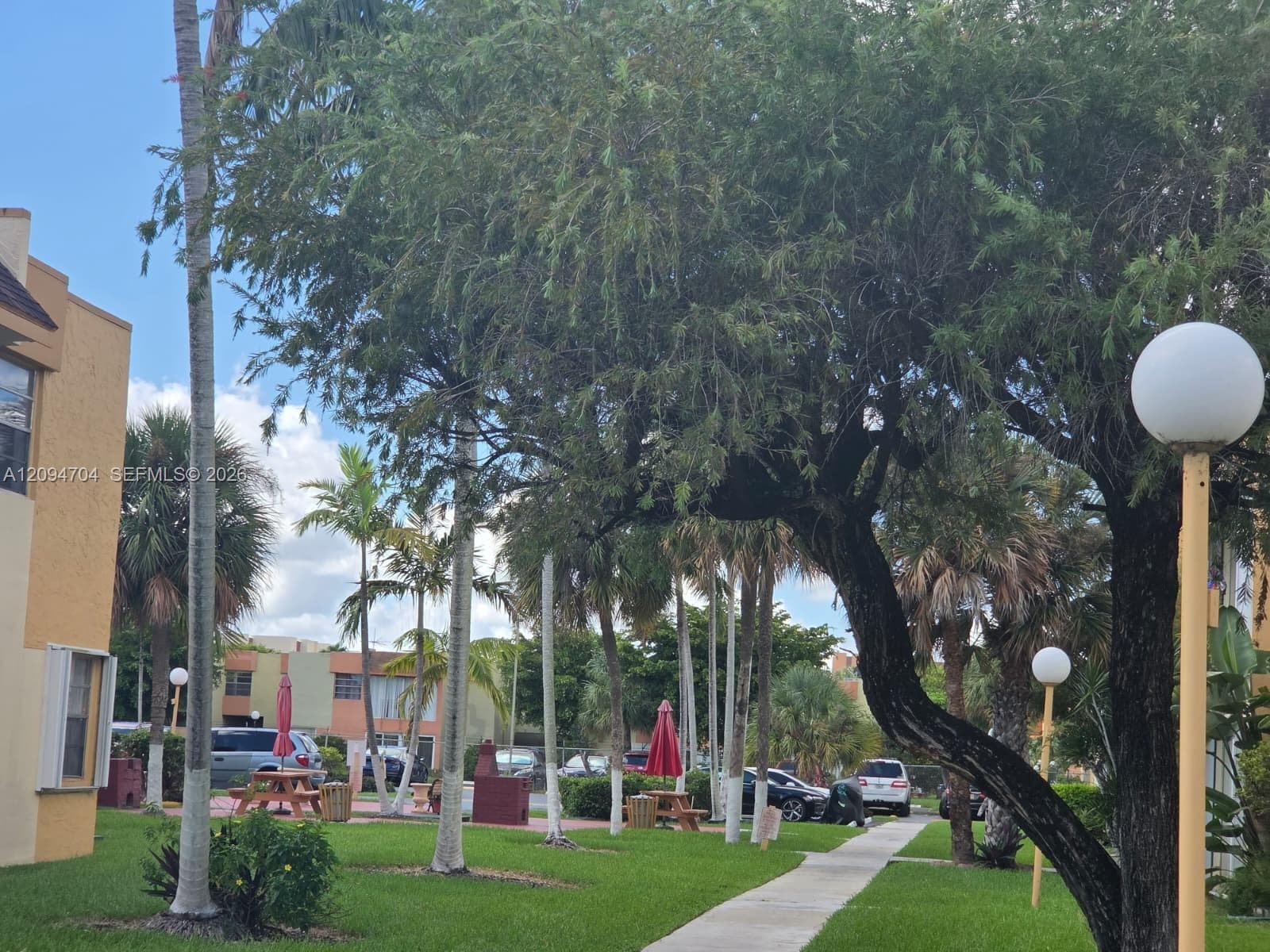Landscaped grounds featuring mature trees, manicured lawns, paved walkways, and globe-style exterior lighting