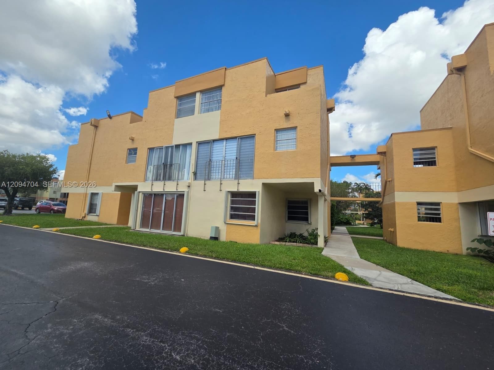 Multi-level stucco exterior featuring balcony access, horizontal sliding windows, and a paved walkway