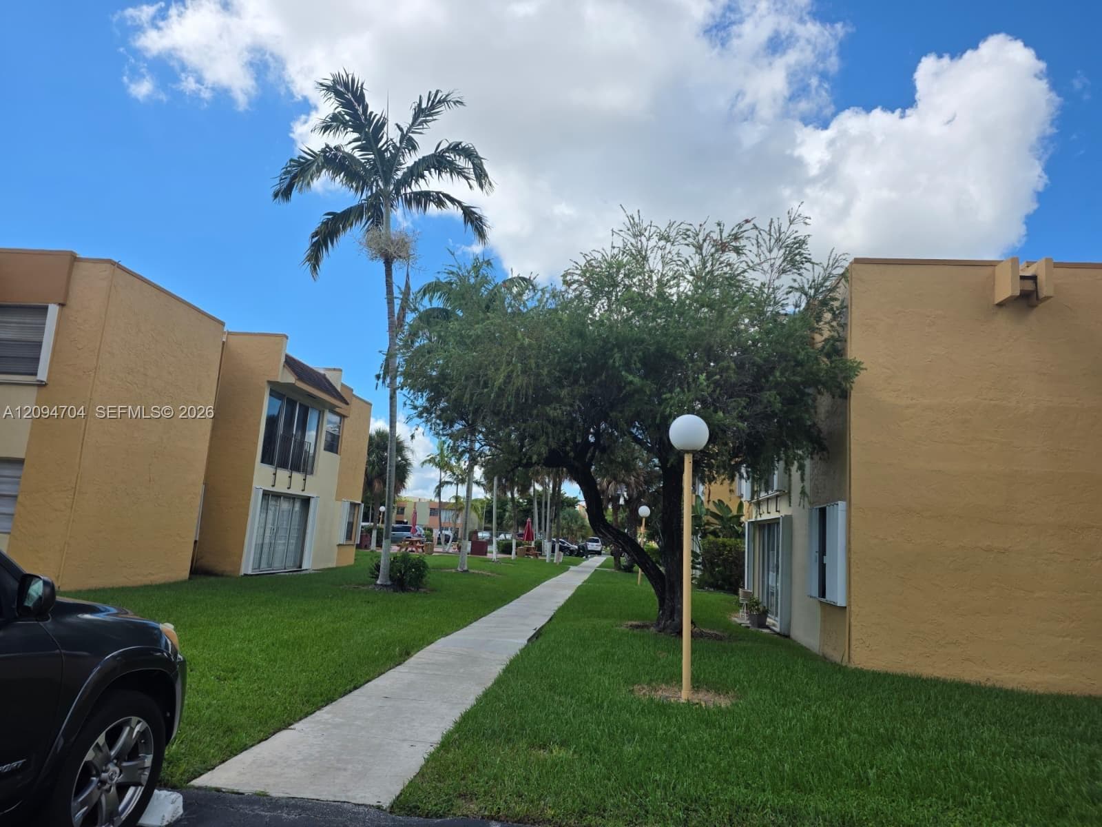 Stucco exterior buildings featuring concrete walkways, manicured lawn, mature palm trees, and outdoor globe lighting