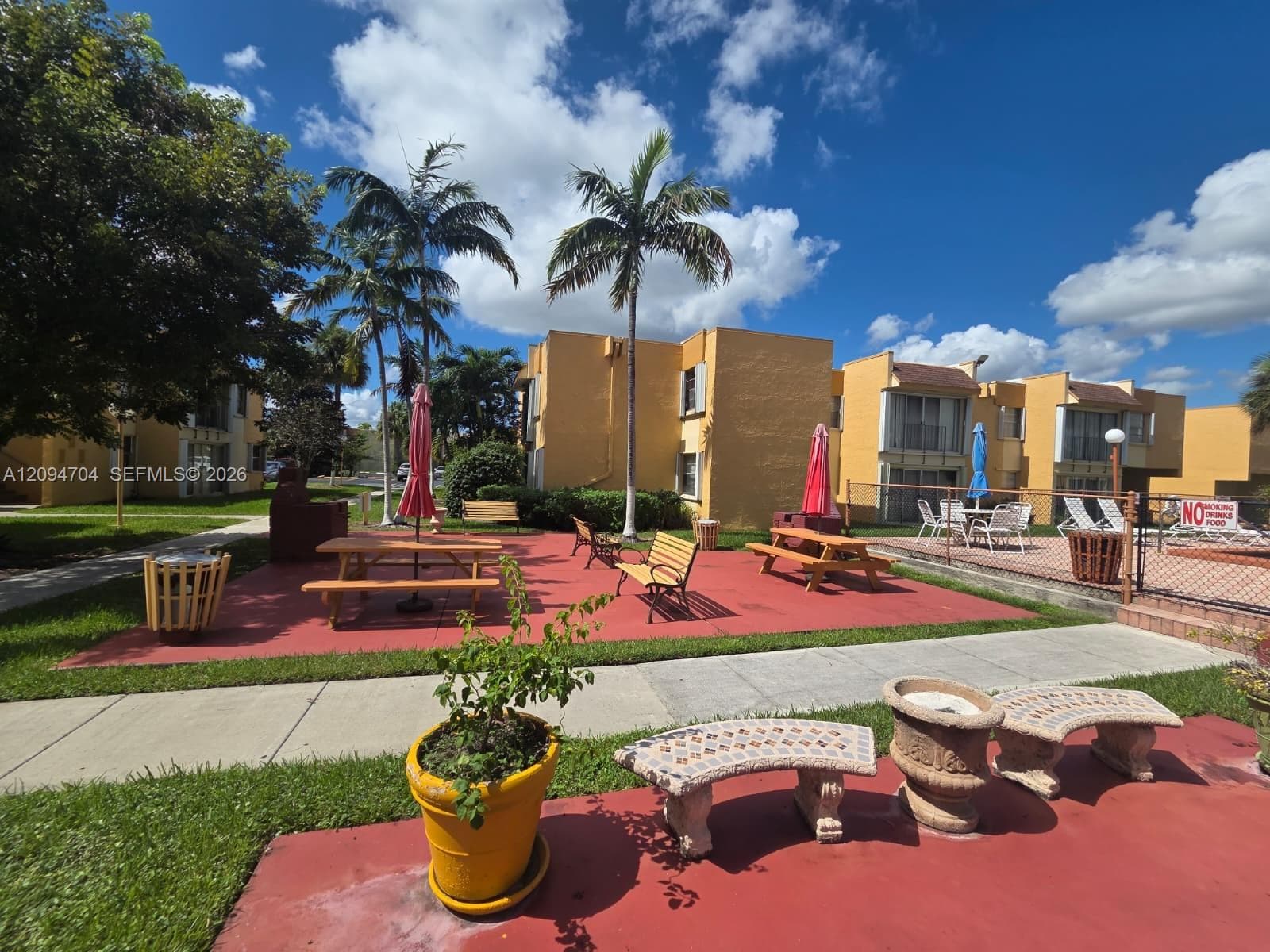 Community patio featuring red paved surfacing, concrete benches, and mature palm trees