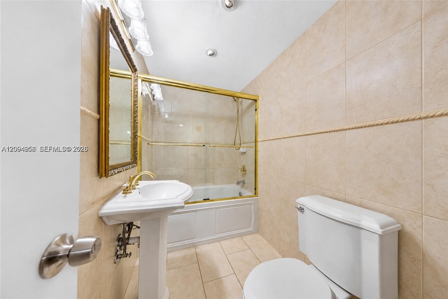 Full-height ceramic wall tiling, pedestal sink with gold-tone hardware, gold-framed glass shower enclosure with integrated tub, and ceramic floor tiling