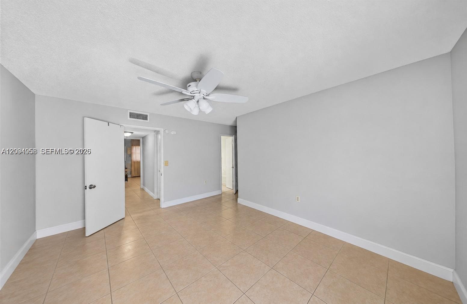 Neutral interior room featuring large-format ceramic tile flooring, a multi-blade ceiling fan with integrated lighting, and solid-core interior doors