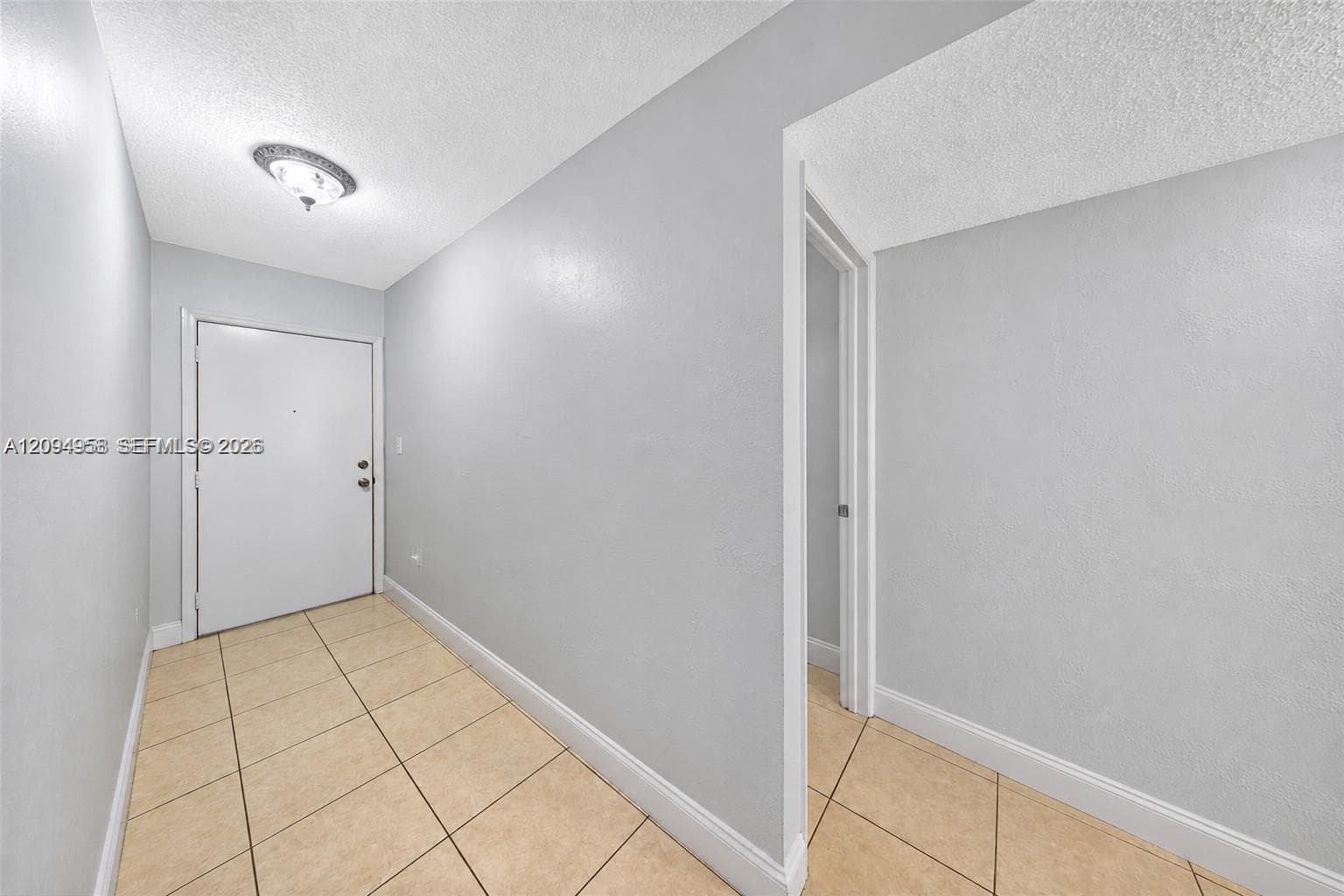 Neutral-toned entryway featuring large-format ceramic tile flooring, a solid-panel door with metallic hardware, and a flush-mount ceiling light fixture