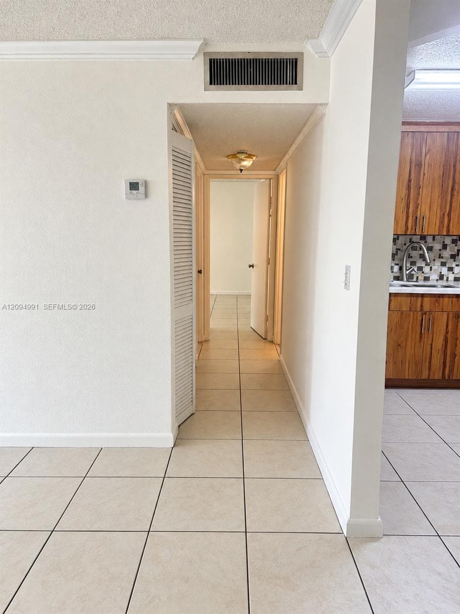 Neutral-toned tile flooring, louvered closet door, and wood-finish cabinetry with a patterned tile backsplash