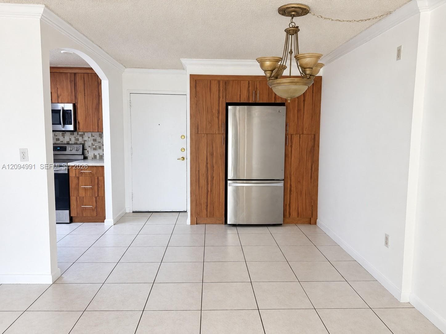Ceramic tile flooring, crown molding, built-in wood-finish cabinetry, stainless steel refrigerator, and traditional chandelier