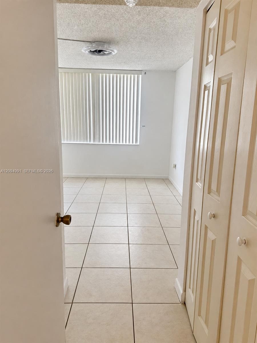 Room featuring neutral tile flooring, bi-fold closet doors, vertical window blinds, and a ceiling-mounted light fixture