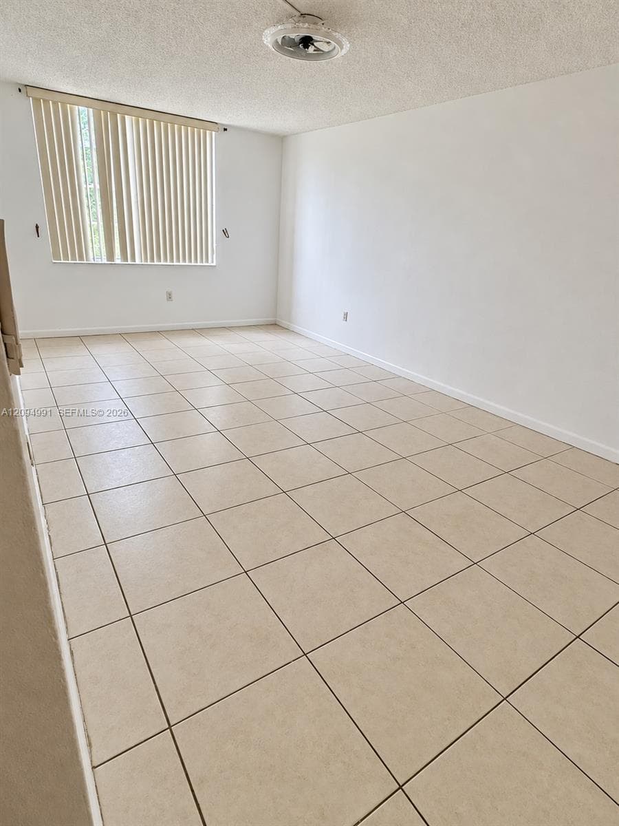 Neutral-toned ceramic tile flooring, clean white walls, textured ceiling, and vertical window blinds
