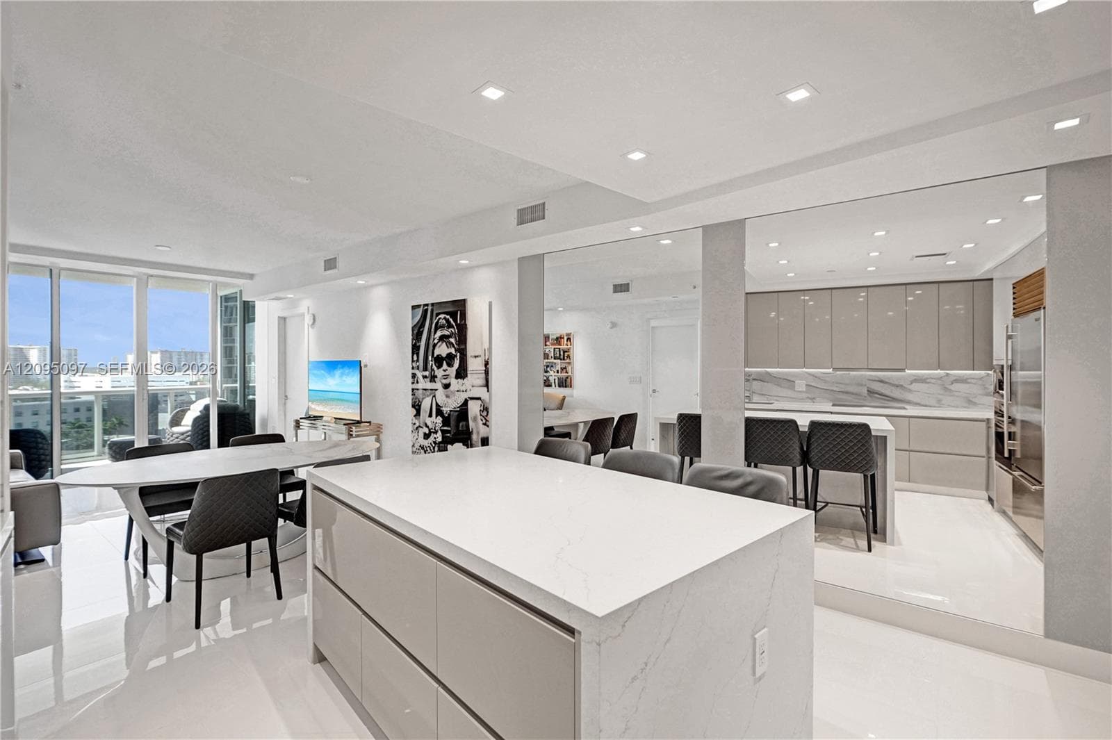 Open-concept interior featuring high-gloss cabinetry, a central island with a solid surface countertop, stone-finish backsplash, recessed ceiling lighting, and floor-to-ceiling windows