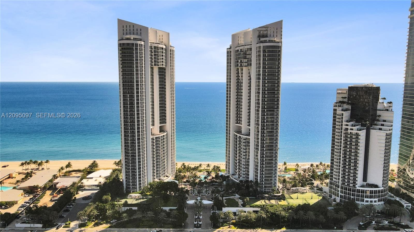 High-rise residential towers featuring expansive floor-to-ceiling glass paneling and private balconies, situated on a coastal site with direct oceanfront access and meticulously landscaped grounds